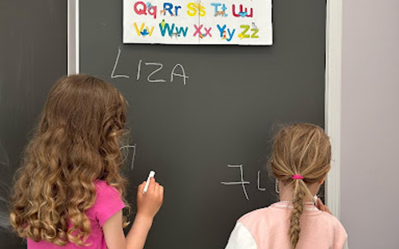 Zwei Kinder schreiben an einer Tafel und entdecken Buchstaben und Zahlen